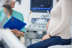 Pregnant woman and doctor in a consultation in doctor's office, ultrasound in background